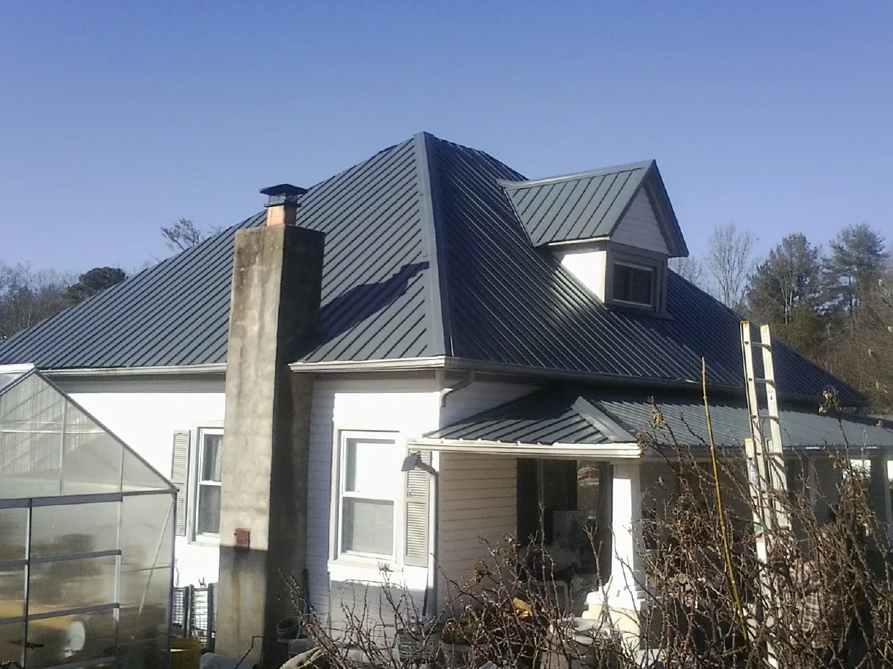 Dark blue standing seam metal roof on a white farmhouse with dormer — Slate & Tile Roof Repair by Roofing Brothers in Andersonville
