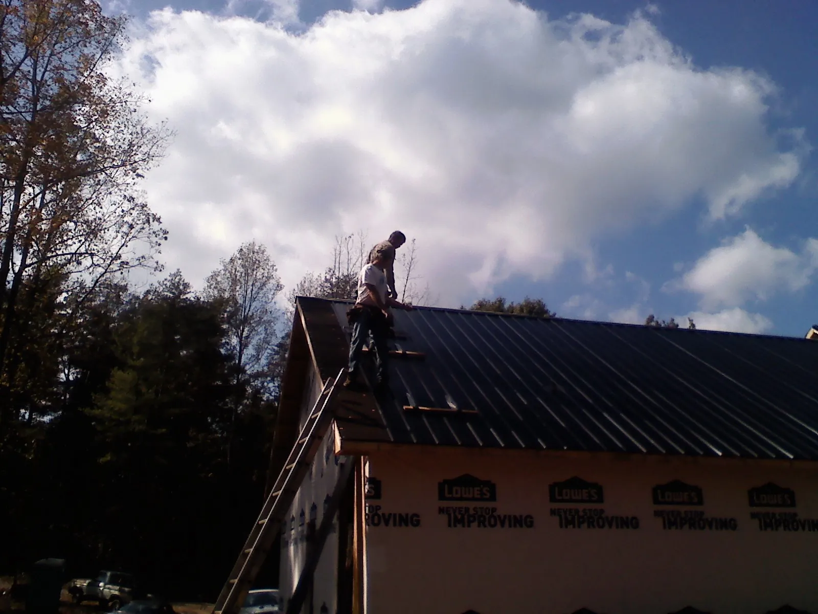 Roofer fastening dark metal panels high against a cloudy sky, from a Roof Inspection job in Andersonville