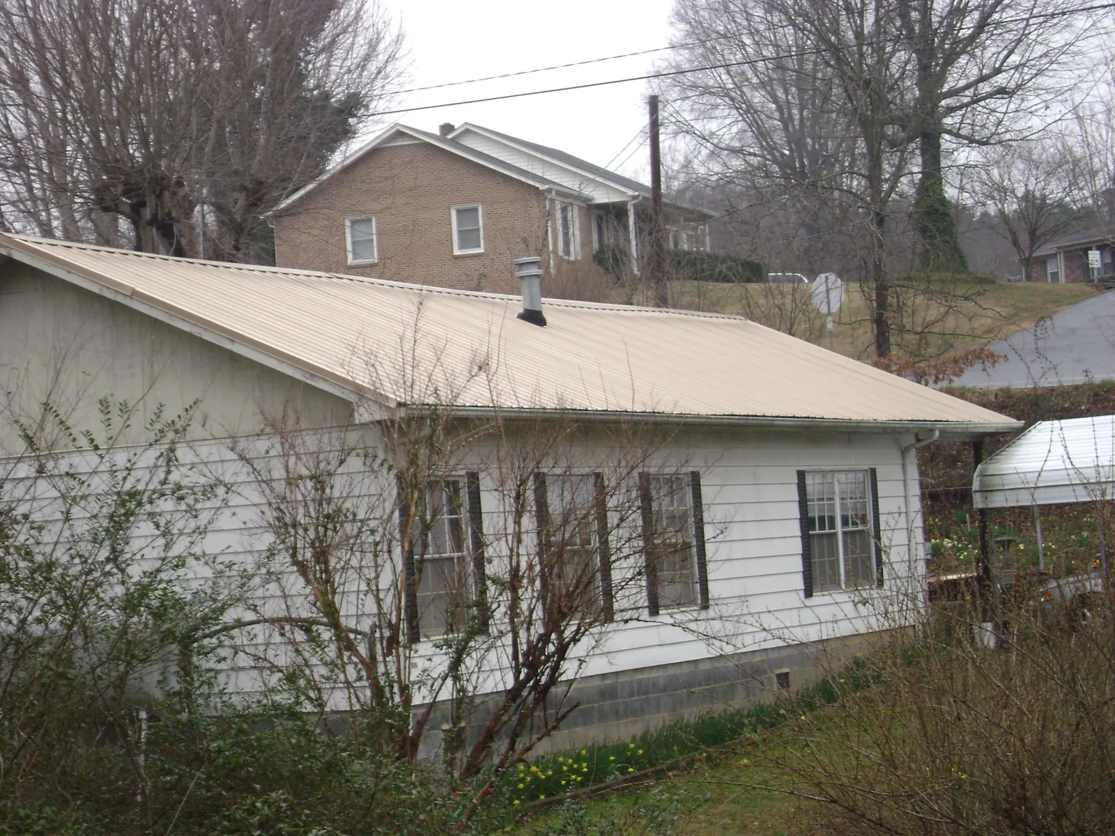 Tan metal roof on a white sided house set into a hillside — Commercial Roofing by Roofing Brothers in Andersonville